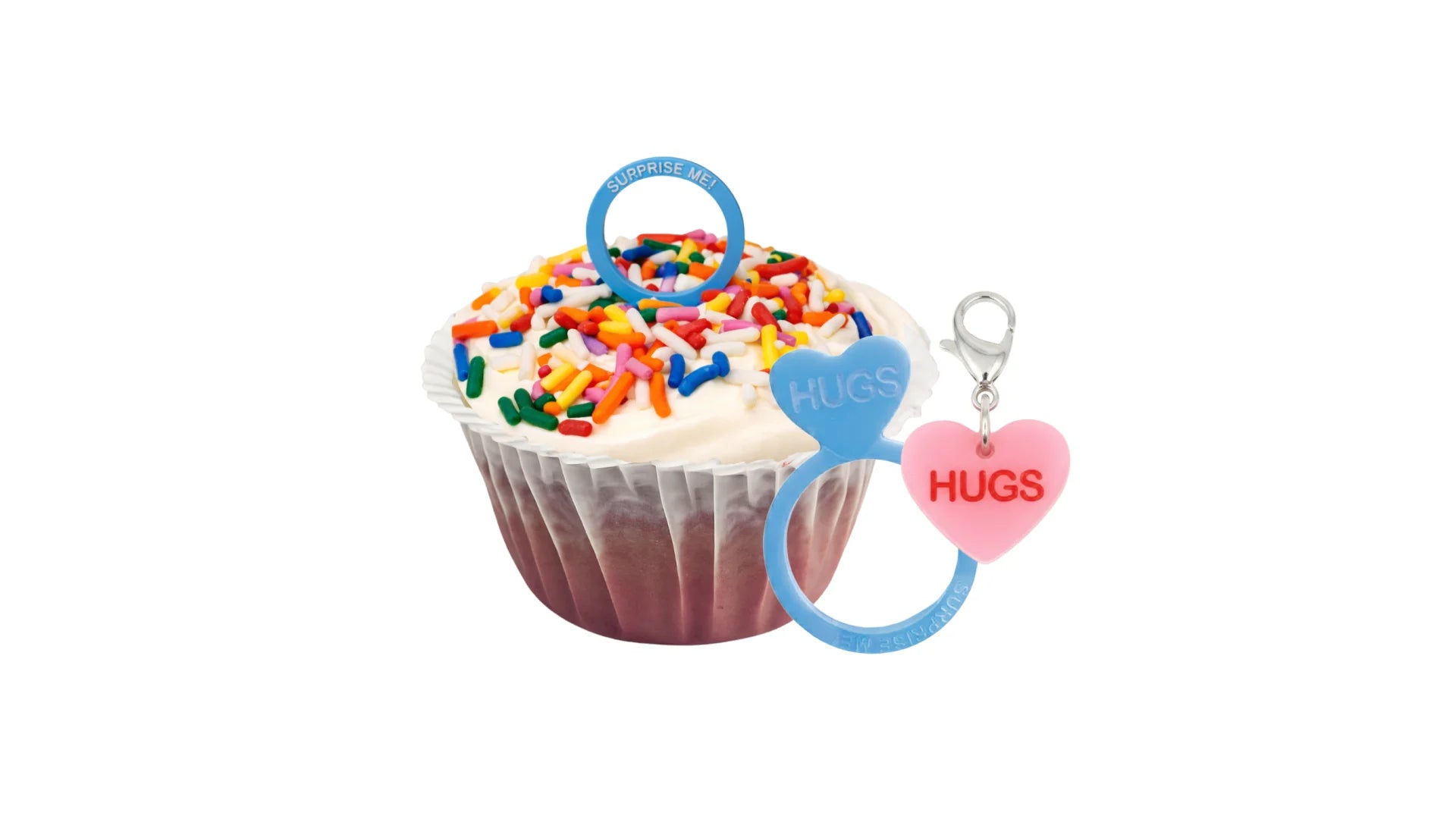 A Red Velvet Cupcake Topped with Marshmallow Whipped Frosting, Rainbow Sprinkles and a Pull-Out Ring with a Message. Comes with a Matching Mini Conversation Heart Charm.