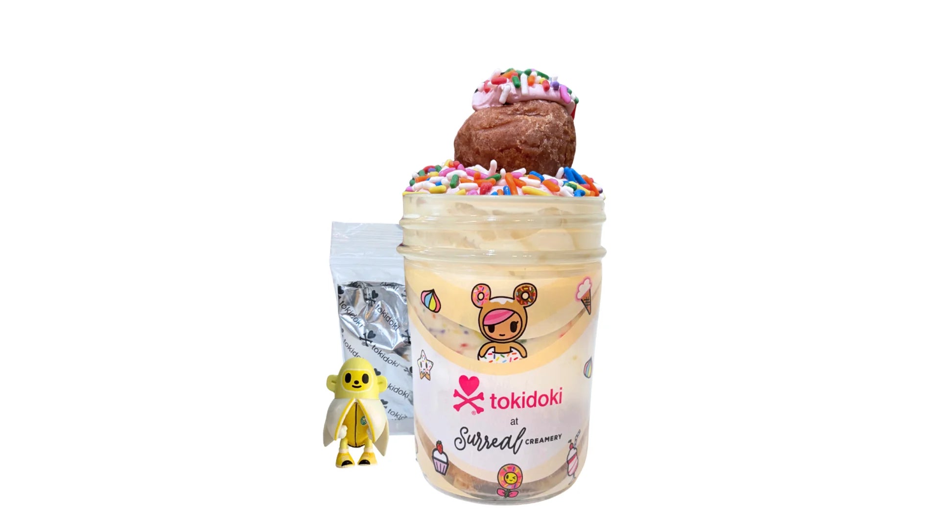 A tokidoki inspired Breaking Batter Cake Jar with Tres Leches Vanilla Cake, Strawberry Frosting, Rainbow Sprinkles and a Frosted Donut Hole with Rainbow Sprinkles. Served in a limited-edition mason jar and paired with one 1" tokidoki mystery collectible.